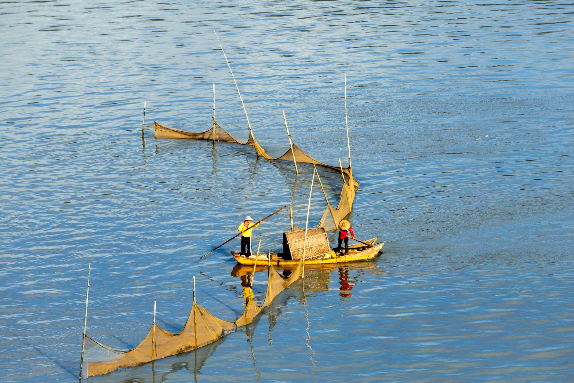 Dwóch rybaków łowi tradycyjnie sieciami na spokojnej rzece