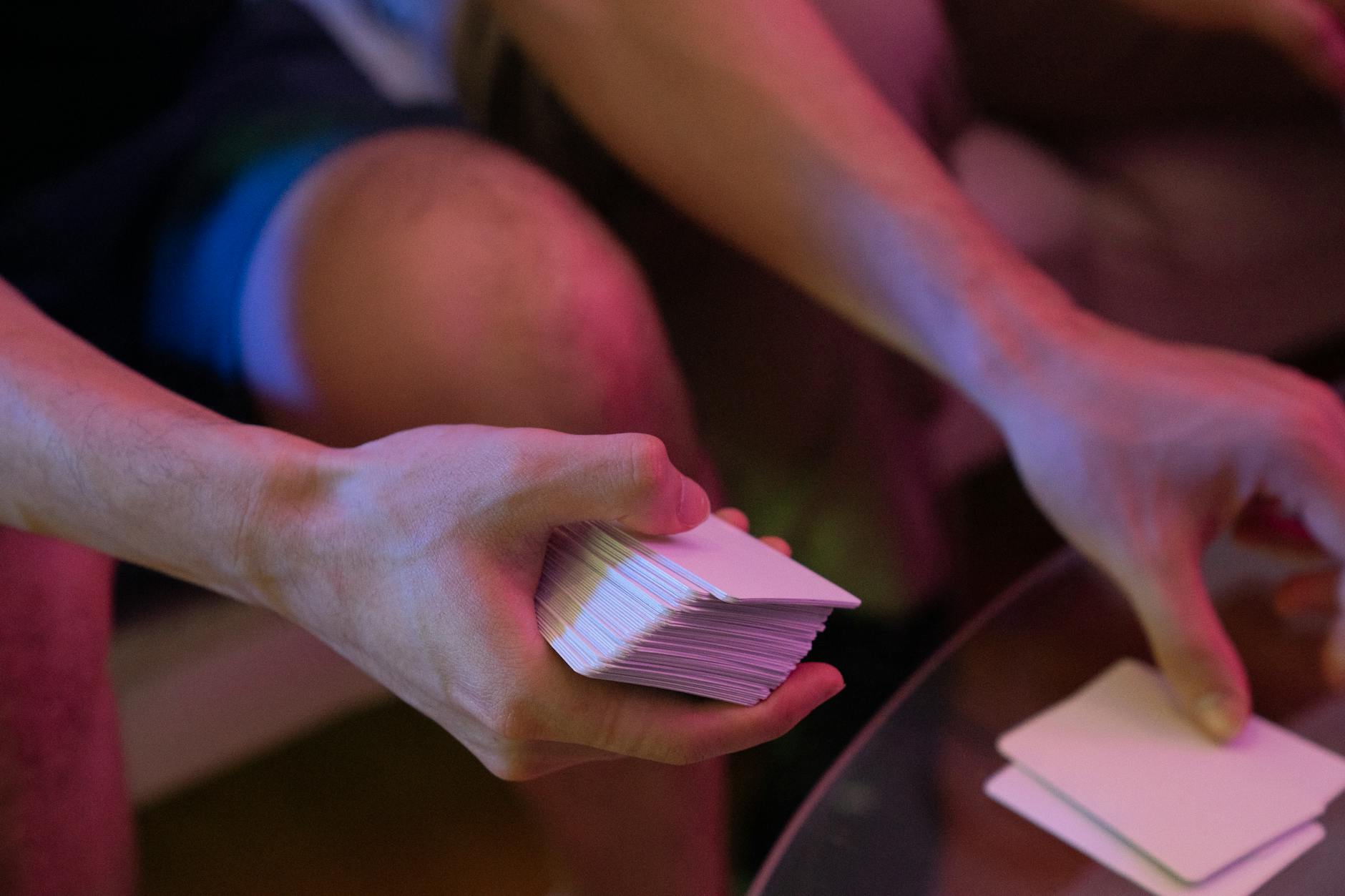 Ręce tasujące talię kart na szklanym stole w różowym świetle