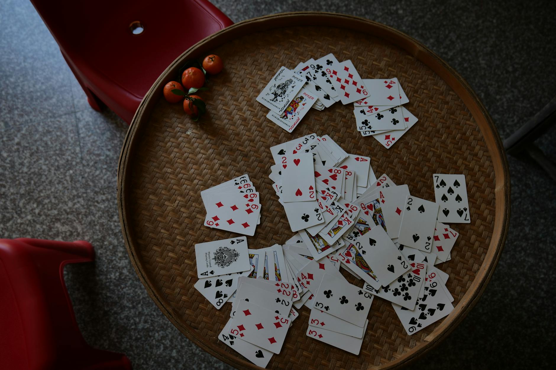 Rozsypane karty do gry na wiklinowym stole z czerwonymi krzesłami